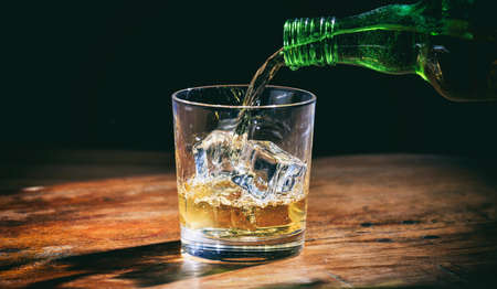 Pouring whiskey in a glass on wooden backgroundの写真素材