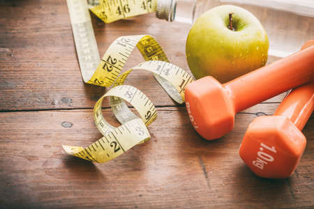 Green apple, dumbbells and measuring tape on wooden backgroundの写真素材