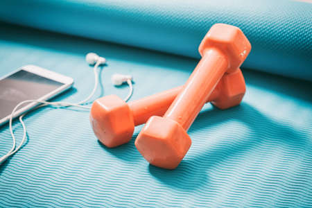 Dumbbells and a smartphone on a green yoga matの写真素材