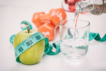 Green apple, water and dumbbells on white backgroundの写真素材