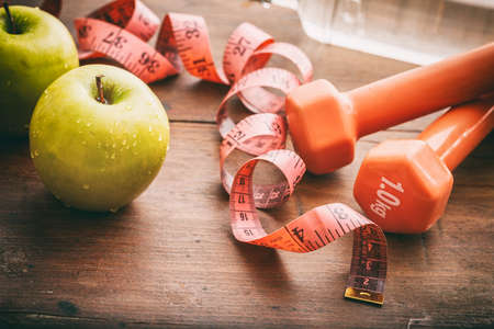 Green apples, dumbbells and measuring tape on wooden backgroundの写真素材