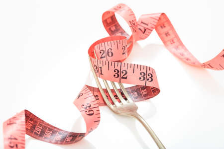 Pink measuring tape and a fork on white backgroundの写真素材