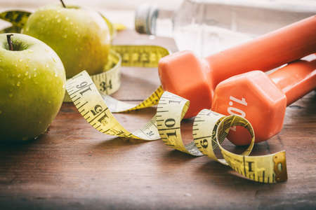 Green apples, dumbbells and measuring tape on wooden backgroundの写真素材