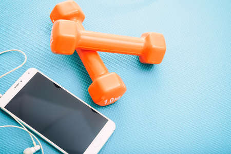 Dumbbells and smartphone on a green yoga mat