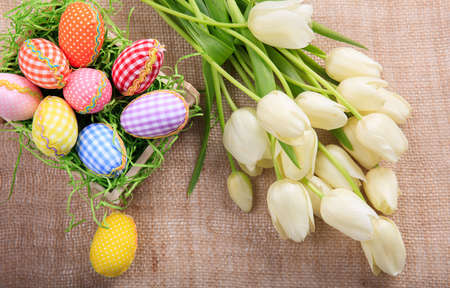 Colorful Easter eggs and white tulips on a burlapの写真素材