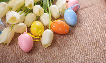 Colorful Easter eggs and white tulips on a burlapの写真素材