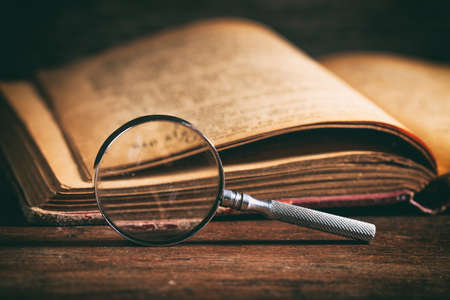 Vintage book and magnifying glass on wooden backgroundの写真素材
