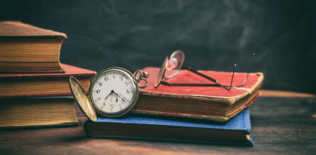 Vintage books and pocket watch on a wooden deskの写真素材
