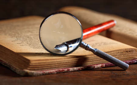 Ink pen and magnifying glass on a vintage bookの写真素材