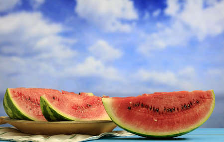 Ripe watermelon slices on a wooden table - blue sky background - copy spaceの写真素材