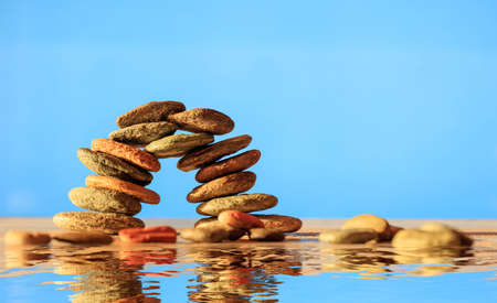 Zen stones stacked on blue background, reflections on the waterの写真素材