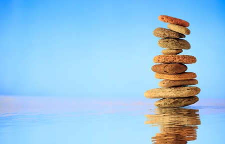 Zen stones stacked on blue background, reflections on the waterの写真素材