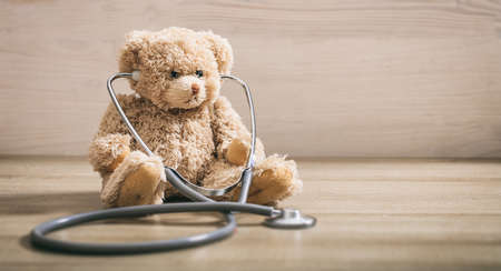 Teddy bear with a heart stethoscope sitting on a wooden backgroundの写真素材