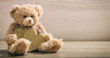 Teddy bear holding golden hearts on wooden backgroundの写真素材