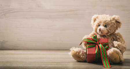 Teddy bear holding a gift on wooden backgroundの写真素材