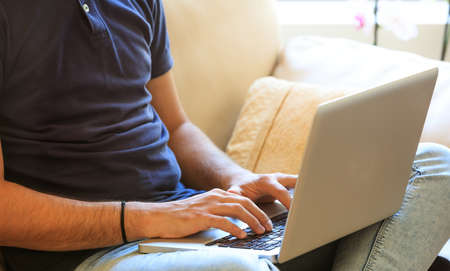Young man working with a laptop sitting on a sofa at homeの写真素材