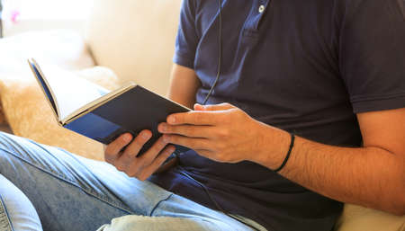 Young man reading a book sitting on a sofa at homeの写真素材