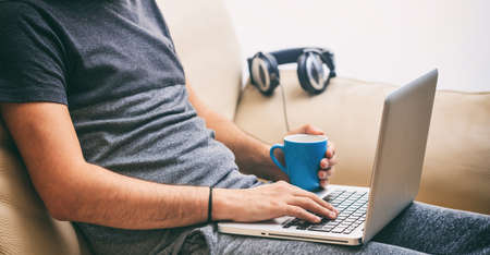 Young man working with a laptop sitting on a sofa at homeの写真素材