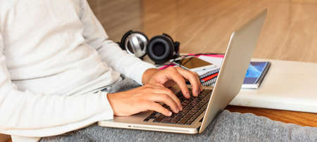 Young man working with a laptop sitting on wooden floor at homeの写真素材