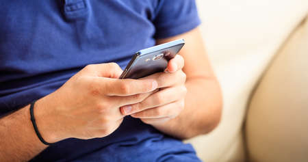 Young man looking at his smart phone, closeup on the handsの写真素材