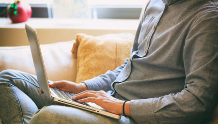 Young man working with a laptop sitting on a sofa at homeの写真素材