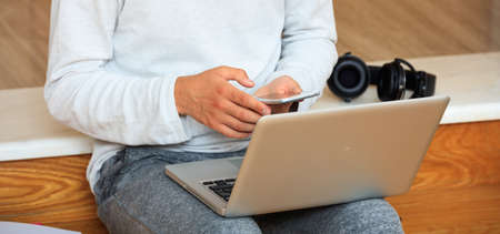Young man looking at his smart phone, sitting on wooden floorの写真素材