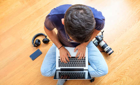 Modern workspace at home. Young man with a laptop and a camera on the wooden floor. Top viewの写真素材