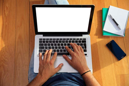 Modern workspace at home. Young man working with a white screen laptop on the wooden floor. Top view, copy spaceの写真素材