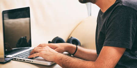 Young man working with a laptop sitting on a sofa at homeの写真素材