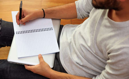 Modern workspace at home. Young man making notes, sitting on wooden floorの写真素材