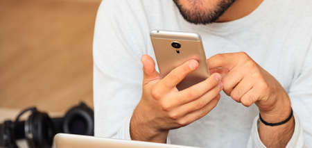 Young man looking at his smart phone, closeup on the hands