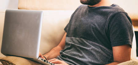 Young man working with a laptop sitting on a sofa at homeの写真素材