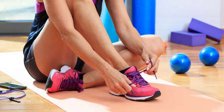 Woman in a fitness class, tying the shoe laces on wooden floorの写真素材