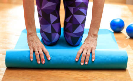 Fitness at home concept. Woman rolling an exercise mat on wooden floorの写真素材