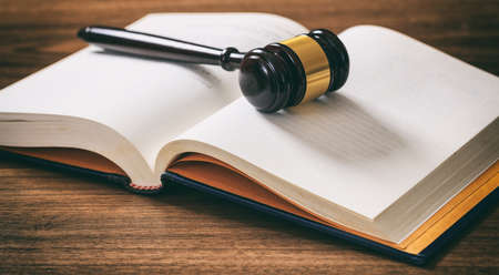 Law or auction gavel on an open book, wooden desk, dark background