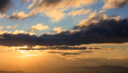 Beautiful sunset on colorful sky. Gold sun lightens the clouds over mountains. Sun on the left side.の写真素材