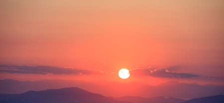 Beautiful sunset on orange sky over mountains background. The sun is in the middle.の写真素材