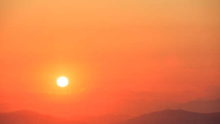 Beautiful sunset on orange sky over mountains background. The sun is on the left side.の写真素材