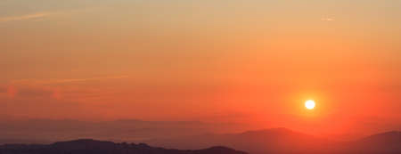 Beautiful sunset on orange sky over mountains background. The sun is on the right side.の写真素材