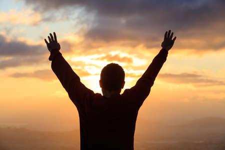 Silhouette of man standing with open hands looking at the golden sun. Peaceful view.の写真素材