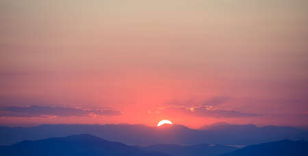 Beautiful sunset on orange sky over mountains background. The sun is in the middle.の写真素材