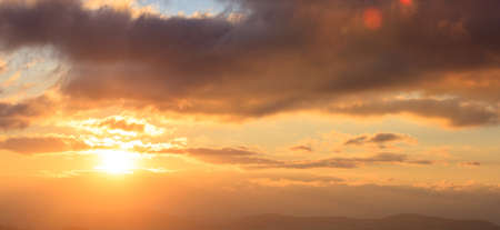 Beautiful sunset on colorful sky. Gold sun lightens the clouds over mountains. Sun on the left side.の写真素材