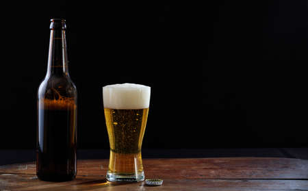 A bottle and a glass of beer on a wooden table, dark background. Copy spaceの写真素材