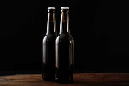Closeup of two unopened beer bottles isolated on a wooden bench, black backgroundの写真素材