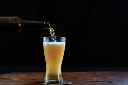 Pouring beer in a glass on a wooden table, dark background. Copy spaceの写真素材