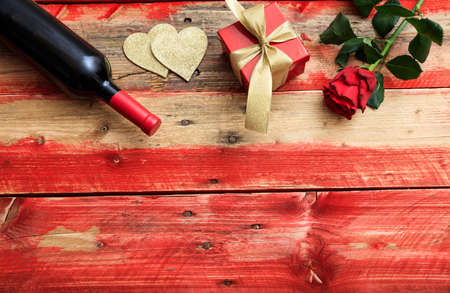 Valentines day concept. Red wine bottle, rose and a gift on wooden backgroundの写真素材
