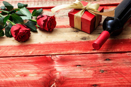 Valentines day concept. Red wine bottle, roses and a gift on wooden backgroundの写真素材
