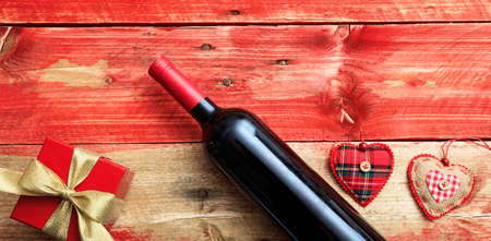 Valentines day concept. Red wine bottle, a gift box and hearts on red wooden backgroundの写真素材