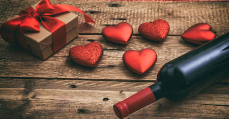 Valentines day concept. Red wine bottle, a gift box and hearts on wooden backgroundの写真素材