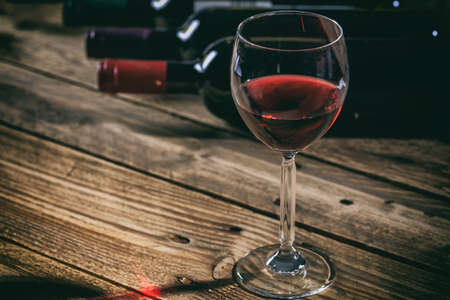 Red wine glass on a wooden table, wine bottles collection backgroundの写真素材